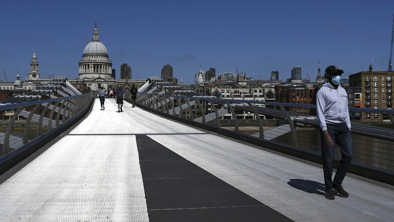 Ein Mann mit Mundschutz überquert die fast menschenleere Millennium Bridge in London.