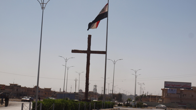 Symbolhaftes Bild in Karakosch: ein meterhohes Holzkreuz und gleich dahinter die Fahne des Irak. 