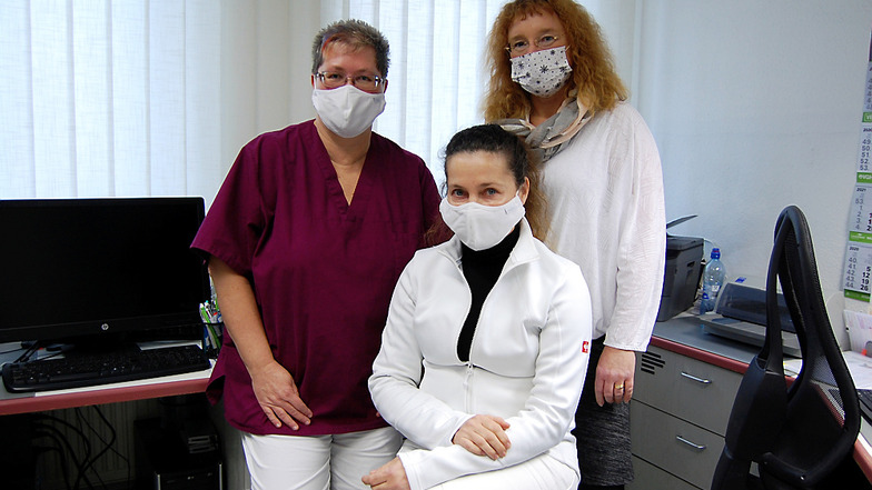 Auch sie müssen mit Mund- Nasen-Bedeckung ausgerüstet sein, wenn sie in der Anmeldung der Praxis die Patienten empfangen. Frau Dr. Elisabeth Petsch, vorn/in der Mitte sitzend, wird flankiert von Schwester Sabine (links) und Schwester Heike (rechts).