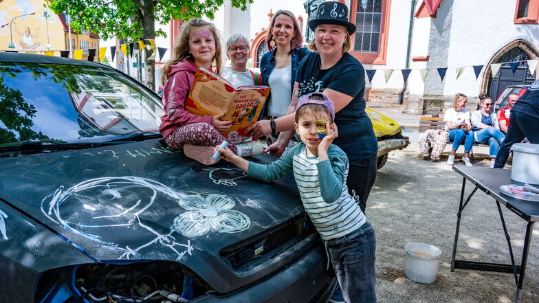 Johannes (7) bemalt das Auto von den Pistenraudis, Joy (7) liest ein Buch über Musik, Sandra Kielau und Oma Margit Kielau freuen sich mit Katja Pietsch von der Bibliothek, dass das Fest bei den Gästen gut ankommt.