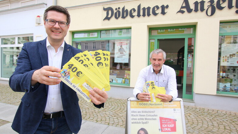 Oberbürgermeister Sven Liebhauser (links) und Matthias Poch, Geschäftsführer der DDV Döbeln GmbH, stehen mit den Gutscheinen vor dem Treffpunkt des Döbelner Anzeigers am Niedermarkt. Ab Freitag gibt es dort die subventionieren Gutscheine zu kaufen.