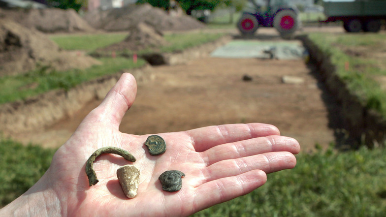 Eine Gewandspange (Bronze), eine Bronzemünze, ein Bleilot und ein Fragment von der Verzierung einer Bronzekanne, die bei Ausgrabungen in Porta Westfalica bei Minden gefunden wurden. 