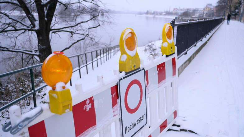 Mit Schnee bedeckt ist ein Schild an einer Absperrung, welches am Ufer der Elbe in Dresden vor Hochwasser warnt.