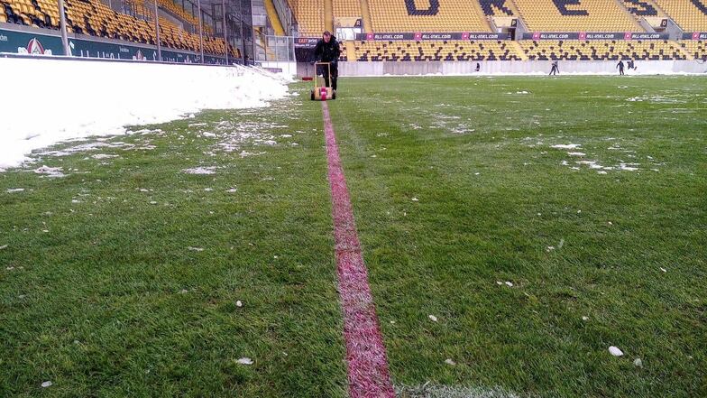 Helfer haben den Rasen im Dresdner Rudolf-Harbig-Stadion vom Schnee beräumt, jetzt werden mit roter Farbe die Linien gezogen.