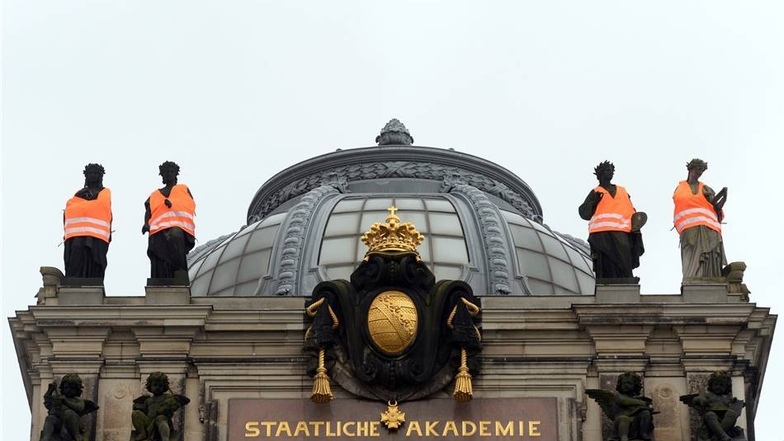 Am Montag hatten Dresdner Kunststudenten unter anderem an der Staatlichen Akademie der Künste die Figuren auf dem Dach  mit Warnwesten versehen. Weiter unten - nicht im Bild - hing zusätzlich ein Banner mit einem Zitat von Johann Wolfgang von Goethe "Das Land, das die Fremden nicht beschützt, geht bald unter".
