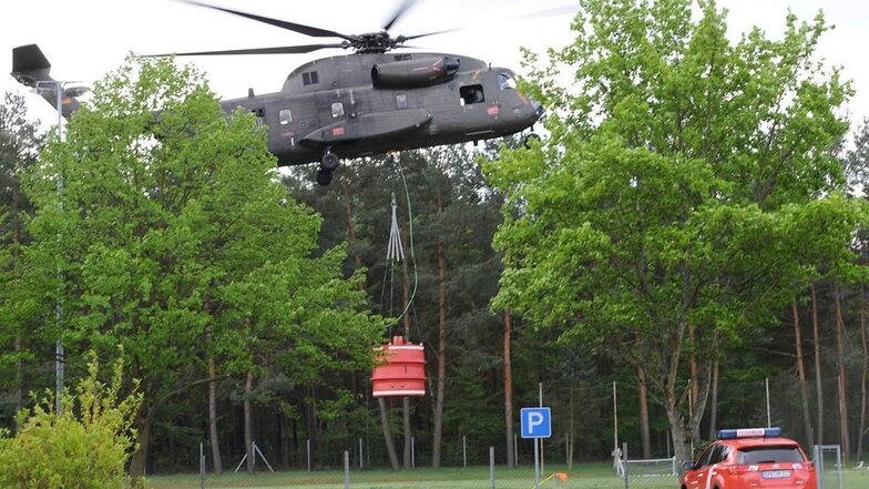 Ein Hubschrauber der Bundeswehr füllt seine Wassertonne auf einem nahegelegenen Sportplatz.