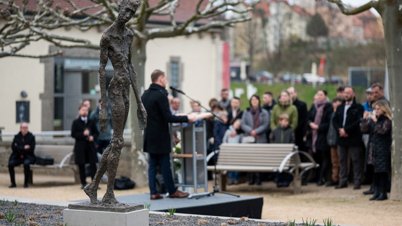 Ministerpräsident Michael Kretschmer spricht hinter der Bronzeplastik „Großer Gehender“ des Künstlers Erik Neukirchner auf der Fläche neben der Altstadtbrücke in Görlitz.