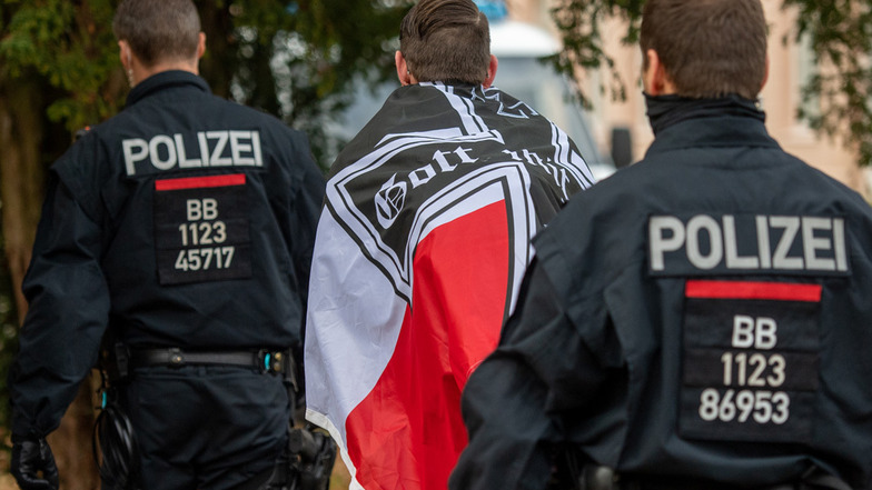 Ein Demonstrant mit einer schwarz-weiß-roten Flagge mit einem Eisernen Kreuz darauf wird von zwei Polizisten abgeführt während einer Demonstration von sogenannten Reichsbürgern.
