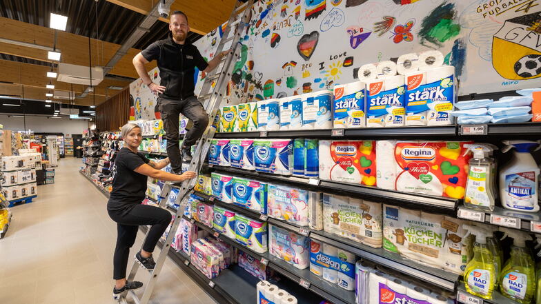 Nicole Theuerkauf (li.) und Marktleiter Patrick Rothe haben das Banner, das beim Public Viewing auf dem Großenhainer Hauptmarkt von Kindern und Erwachsenen bemalt wurde, im Edeka-Markt Scheller aufgehängt.