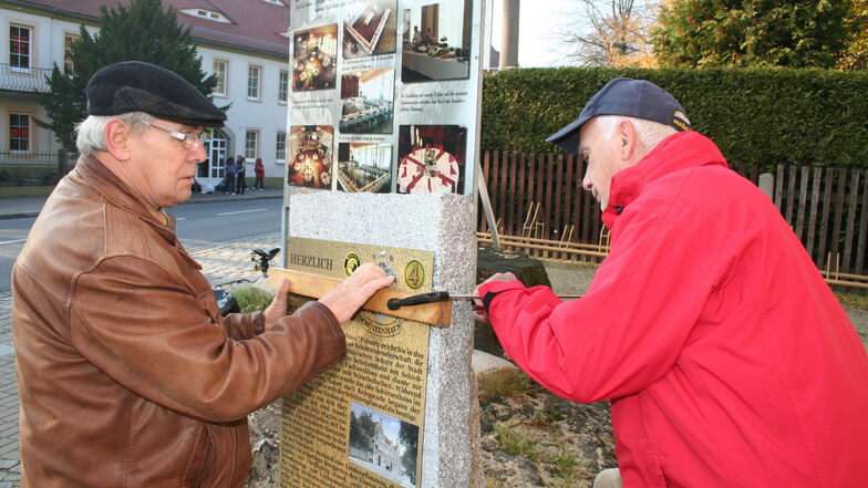 Die Heimatvereinsmitglieder Hartmut Hermann (l.) und Manfred Voit befestigen eine Informationstafel auf einem der historischen Wegesteine in Pulsnitz.