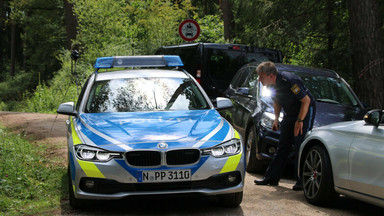 14.07.2019, Bayern, Lauf: Ein Polizist steht auf einem Waldweg an einem Einsatzfahrzeug der Polizei. Ein Pilzsammler hatte zuvor in dem Wald im Landkreis Nürnberger Land einen toten Mann gefunden.