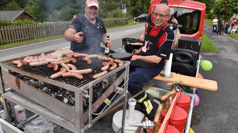Bernd Hering (rechts) und Tilo Dettler von der Schlottwitzer Feuerwehr waren am Sonnabend mit einem mobilen Grill unterwegs. An mehreren Stellen im Ort machten sie Station, um Bratwürste für einen guten Zweck zu verkaufen.