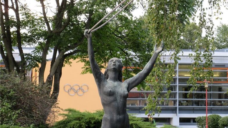 Ostmoderne trifft auf westlichen Zweckbau. Die Statue der Gymnastin steht vor der neu errichteten, mit den olympischen Ringen versehenen Mensa.