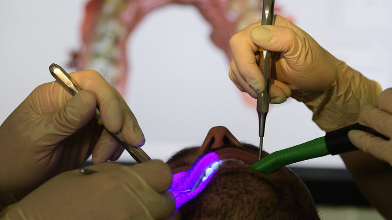 Zahnarzt Conrad Kühnöl und eine Mitarbeiterin untersuchen in Dresden einen Patienten mit einem Fluoreszierenden Mikroskop in der Zahnarztpraxis.