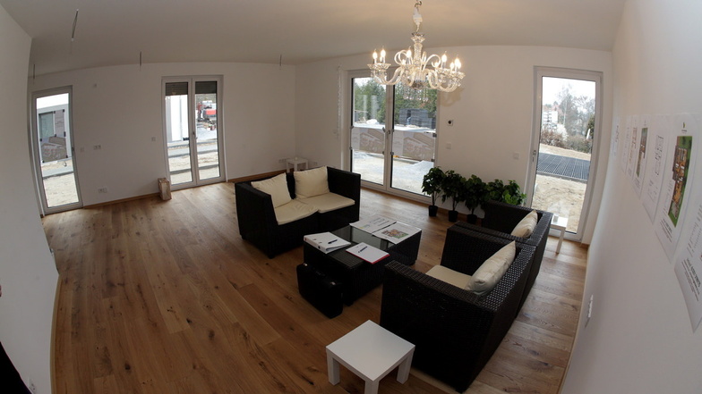Blick ins Wohnzimmer der Musterwohnung. Bodentiefe Fenster mit Jalousien und Echtholz-Parkett.