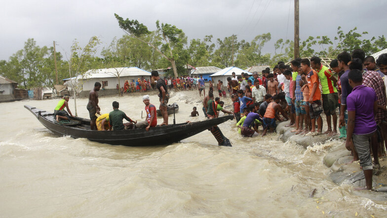 Ein Boot bringt in Shyamnagar (Bangladesch) vor der Ankunft des Zyklons «Amphan» Menschen ans Land, während Einheimische einen Damm überprüfen.
