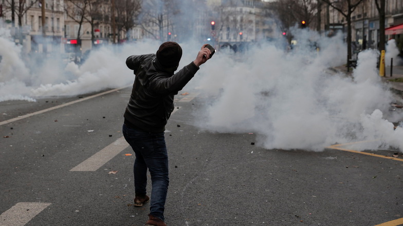 Ein Mann wirft einen Stein in Richtung von Polizeibeamten während eines Protestes nach Schüssen in einem Kulturzentrum in Paris.