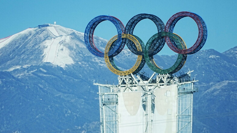 Blick auf olympischen Ringe auf einem Turm in der Yanqing-Region. Im Hintergrund ist der Start der alpinen Olympia-Abfahrt am Xiaohaituo Mountain im Nationalen Ski-Alpin-Zentrum zu sehen.