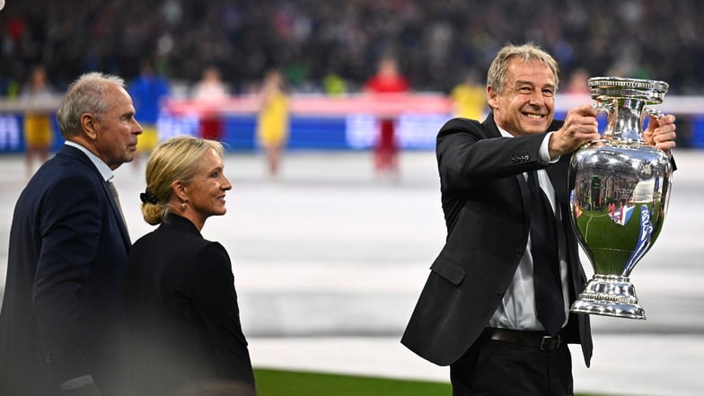 Heidi Beckenbauer (M), steht mit Bernard Dietz (l) und Jürgen Klinsmann, Deutschlands Kapitäne bei den EM-Titeln 1980 und 1996, während Klinsmann den EM-Pokal hält.