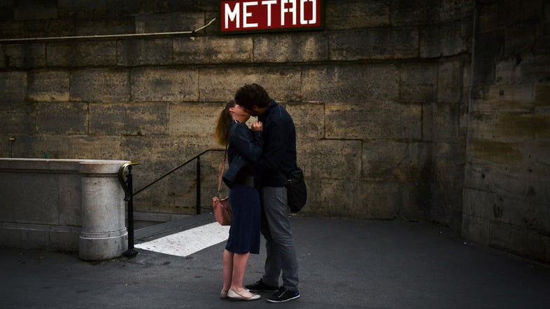 Ein Pärchen küsst sich vor einem Eingang der Pariser Metro.