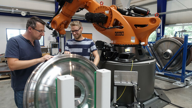 Robert Wallrabe von der Projektleitung und Silvio Müller, verantwortlich für die Software, stehen vor dem Roboter, der die bearbeiteten Räder in Paletten einsortiert.