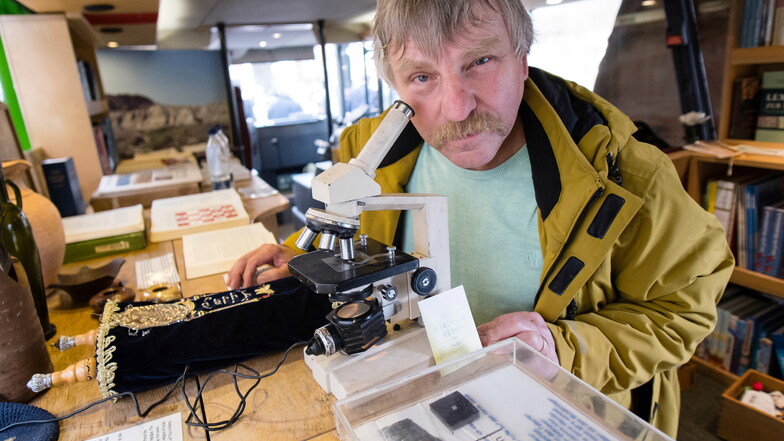 Andreas Schmidt (Mitarbeiter Bibelmobil) im alten Bibelmobil an einem Mikroskop, an dem die kleinste Bibel der Welt betrachtet werden kann.