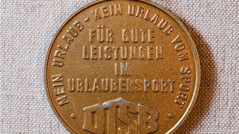 Eine Mediale mit der Aufschrift "Mein Urlaub - Kein Urlaub vom Sport - Für gute Leistungen im Urlaubersport DTSB" aus DDR-Zeiten.