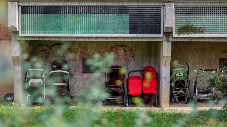 Kinderwagen stehen unter den Balkonen einer Unterkunft für Geflüchtete im Leipziger Stadtteil Grünau. Hier hatte es kürzlich einen Brandanschlag gegeben