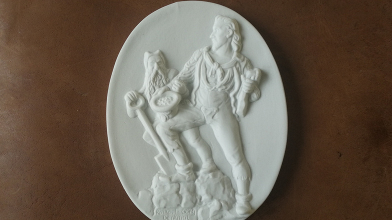 Diese Plakette zeigt die Sagengestalt Rotköpf Görg und einen Gnom. Sie ist das Abbild einer Skulptur im Schlosspark in Freital-Burgk. Gefertigt worden ist die Medaille erst jüngst in der Porzelline mit einer historischen Form.