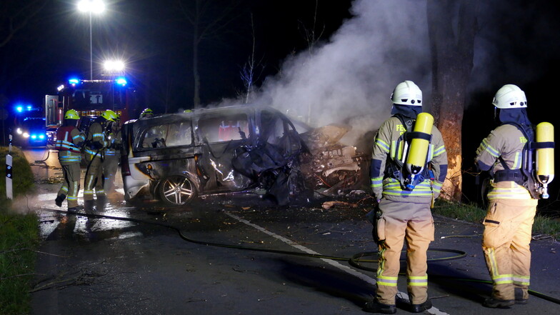 Feuerwehrleute stehen vor dem Wrack eines ausgebrannten Autos, in dem zwei Menschen ums Leben gekommen sind.