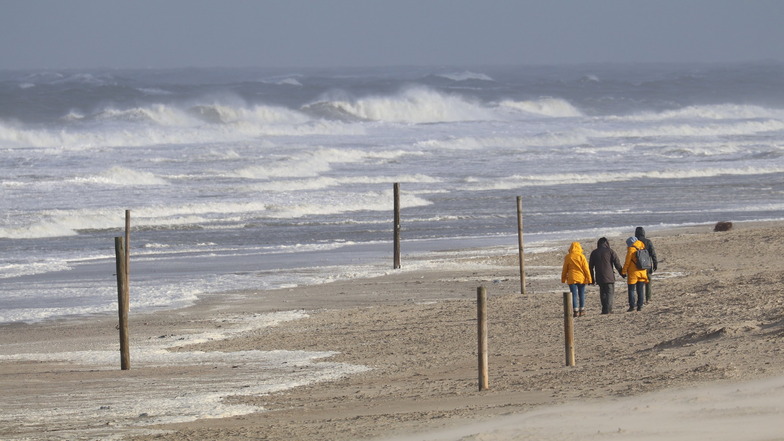 Bei stürmischem Wetter und Wellen gehen Spaziergänger am Strand der ostfriesischen Insel Norderney entlang.