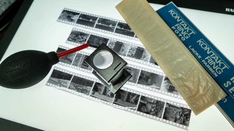 Ein Stillleben mit Fotografen-Utensilien aus schwarz-weißer Zeit: Mit der Lupe wurden die Filmstreifen auf dem Leuchttisch gesichtet und daraus geeignete Negative ausgesucht. Der Pusteball half, Staub zu entfernen.