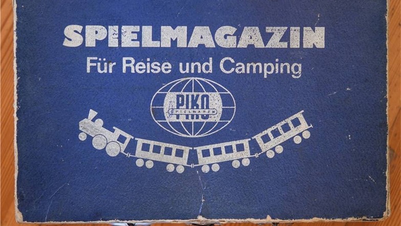 Ein kleiner Koffer mit der Aufschrift für Reise und Camping von PIKO Spielwaren.