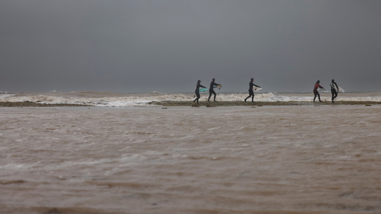 Auch solche Bilder gibt es aus Eckernförde: Surfer gehen über den überfluteten Ostseestrand zum Meer.