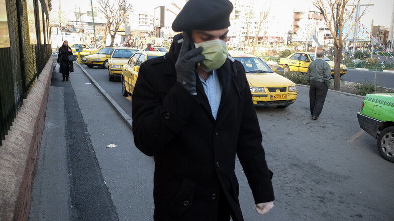 Ein Mann trägt Mundschutz und Handschuhe während er telefonierend eine Straße entlang geht.