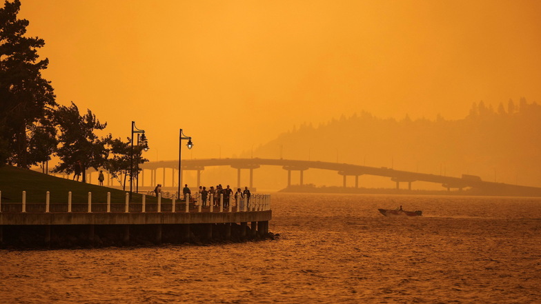 Menschen gehen in Kelowna auf der Promenade spazieren, während der Rauch des McDougall Creek Waldbrandes das Gebiet am Okanagan Lake in Kelowna, British Columbia, bedeckt.