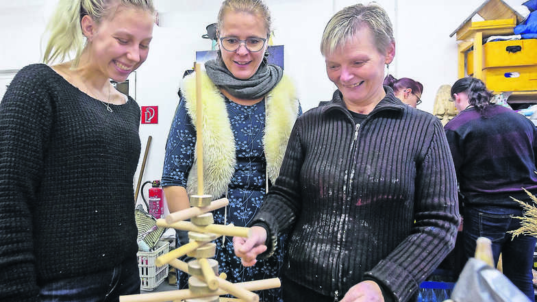 Praktikantin Elisa Heyn, Geschäftsführerin Susanne Beckert und Maßnahmenteilnehmerin Cornelia Bernsdorf (v. l.) schauen sich Holzdeko an, die in der Kreativwerkstatt der Gut Leben angefertigt wurde.