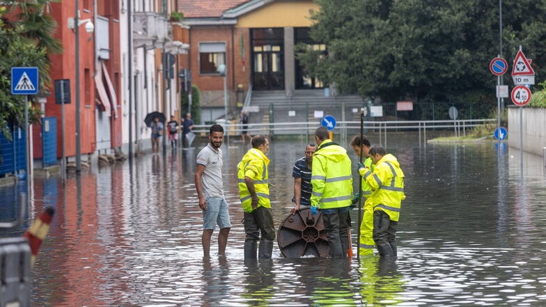 Einsatzkräfte öffnen einen Gullydeckel in Mailand, nachdem ein Unwetter die Straße überflutet hat.