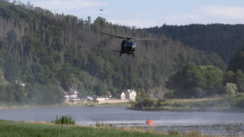 Ein Hubschrauber der Bundeswehr fliegt mit einem Löschwasser-Außenlastbehälter über der Elbe.