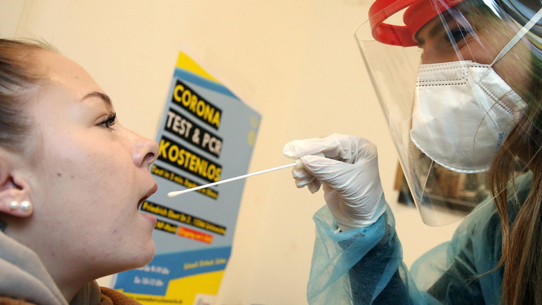 Eine junge Frau lässt von einer Mitarbeiterin einer Corona-Teststelle mit einem Teststäbchen einen Abstrich machen, um sich auf Corona zu testen.