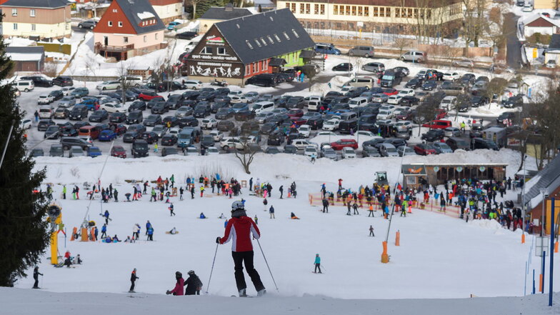 Wintersportfans sind auf dem Altenberger Skihang unterwegs - der Parkplatz ist voll.