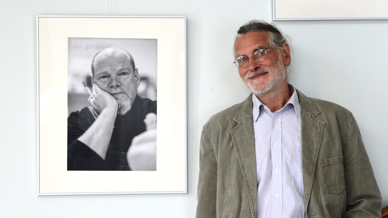 Steffen Petrenz steht im Rathaus Potschappel in seiner Fotoausstellung neben einem Porträt des Porzellankünstlers OIaf Stoy.