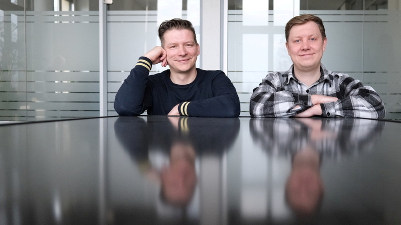 Kay Theuer (l.) und Lukas Hoffmeier, Gründer des Unternehmens Priwatt, sitzen in ihrem Büro und spiegeln sich in der Oberfläche eines Solarmodules.