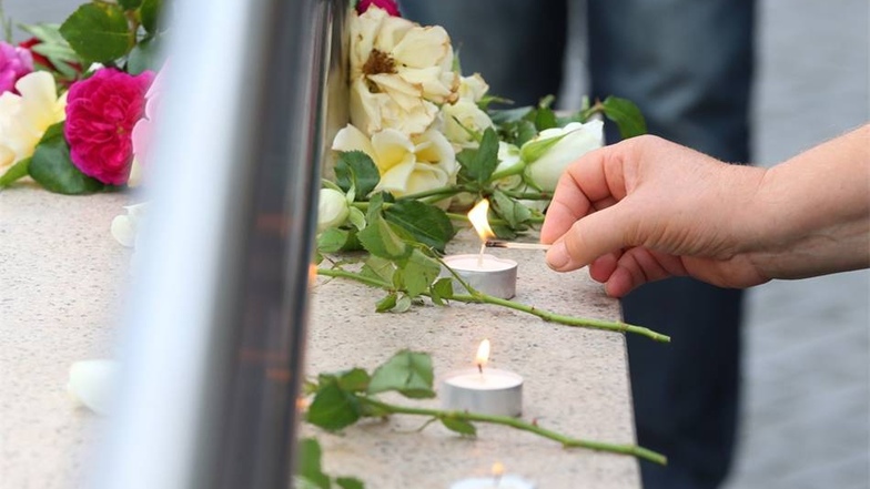 Eine Frau entzündet Kerzen  am Zugang zur U-Bahnstation Olympia-Einkaufszentrum in München (Bayern), den die Polizei nach einer Schießerei mit Toten und Verletzten am Vortag abgesperrt hat.