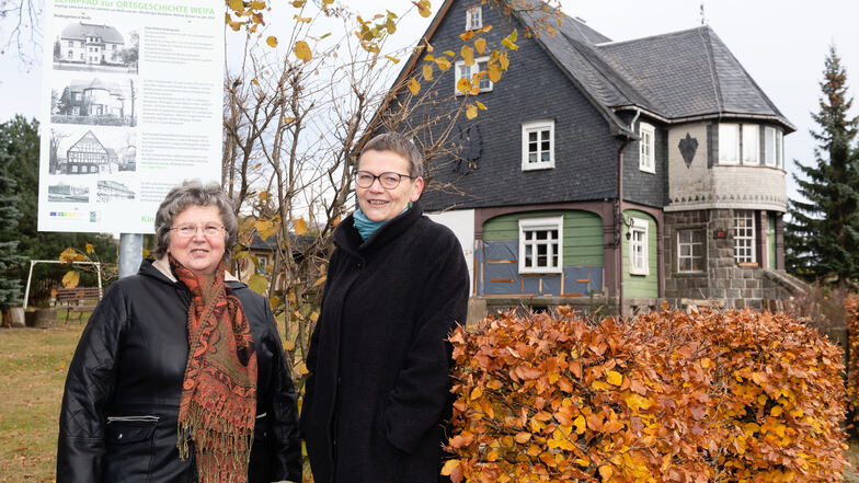 Brigitte Schneider (links) und Kerstin Richter stehen vor einem besonderen Umgebindehaus: Ein Bautzener Jurist ließ es vor rund 100 Jahren als Ferienhaus in Form einer Villa errichten. Ab 1961 befand sich darin der Kindergarten. Eine von 17 Infotafeln ist