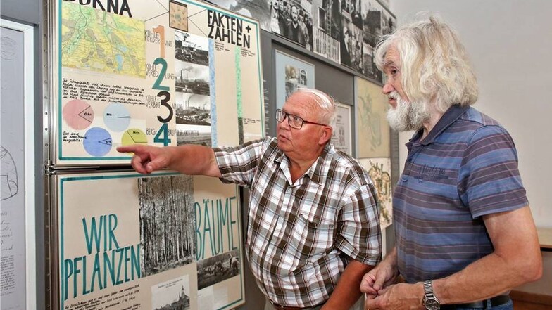 Der ehemalige Pfarrer von Mölbis, Karl-Heinz Dallmann (r), und der ehemalige Bürgermeister Ditmar Haym unterhalten sich vor einer Ausstellungswand über den Wandel des Dorfes.