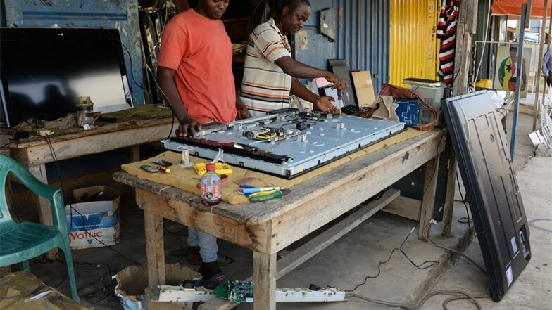 Tony Obour repariert einen Fernseher in seiner Werkstatt in Accra, sein Lehrling schaut ihm dabei über die Schulter