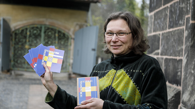 Janet Conrad, Geschäftsführerin der Evangelischen Kulturstiftung Görlitz, steht am Heiligen Grab und zeigt die Startkarten für das neue Geocaching-Spiel. Das Heilige Grab ist die letzte Station, hier ist das Logbuch versteckt, das sie in der Hand hält.