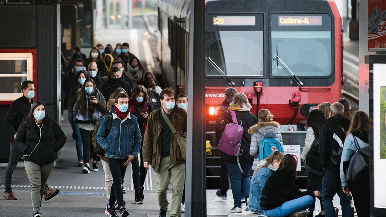 Passagiere mit Mund-Nasen-Schutz gehen am Bahnhof Locarno über den Bahnsteig. Seit Juli 2020 müssen landesweit aufgrund der Corona-Pandemie alle Passagiere in öffentlichen Verkehrsmitteln eine Maske tragen.
