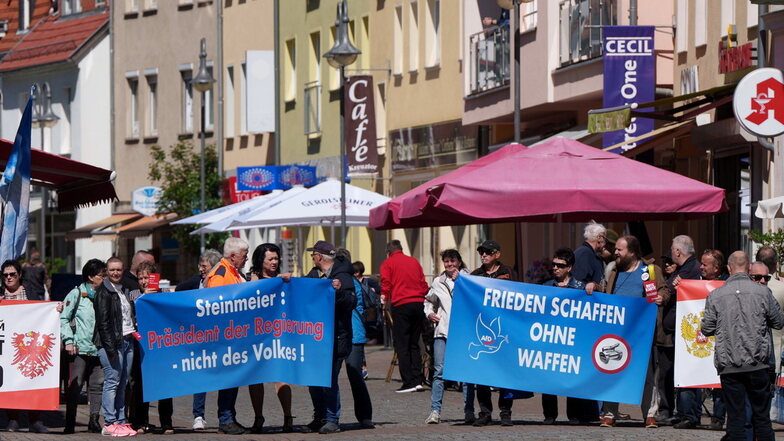 Demonstranten halten vor der Ankunft von Bundespräsident Steinmeier am Rand des Marktplatzes Transparente hoch.